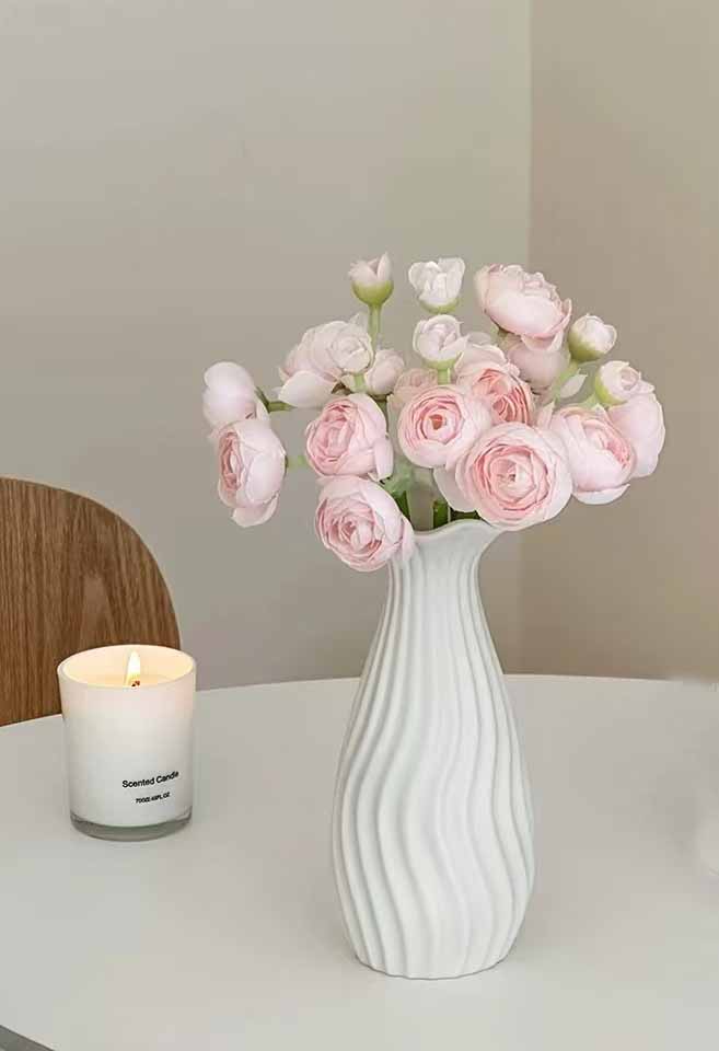 White wavy-textured custom porcelain vase from China with soft pink ranunculus flowers on a modern dining table
